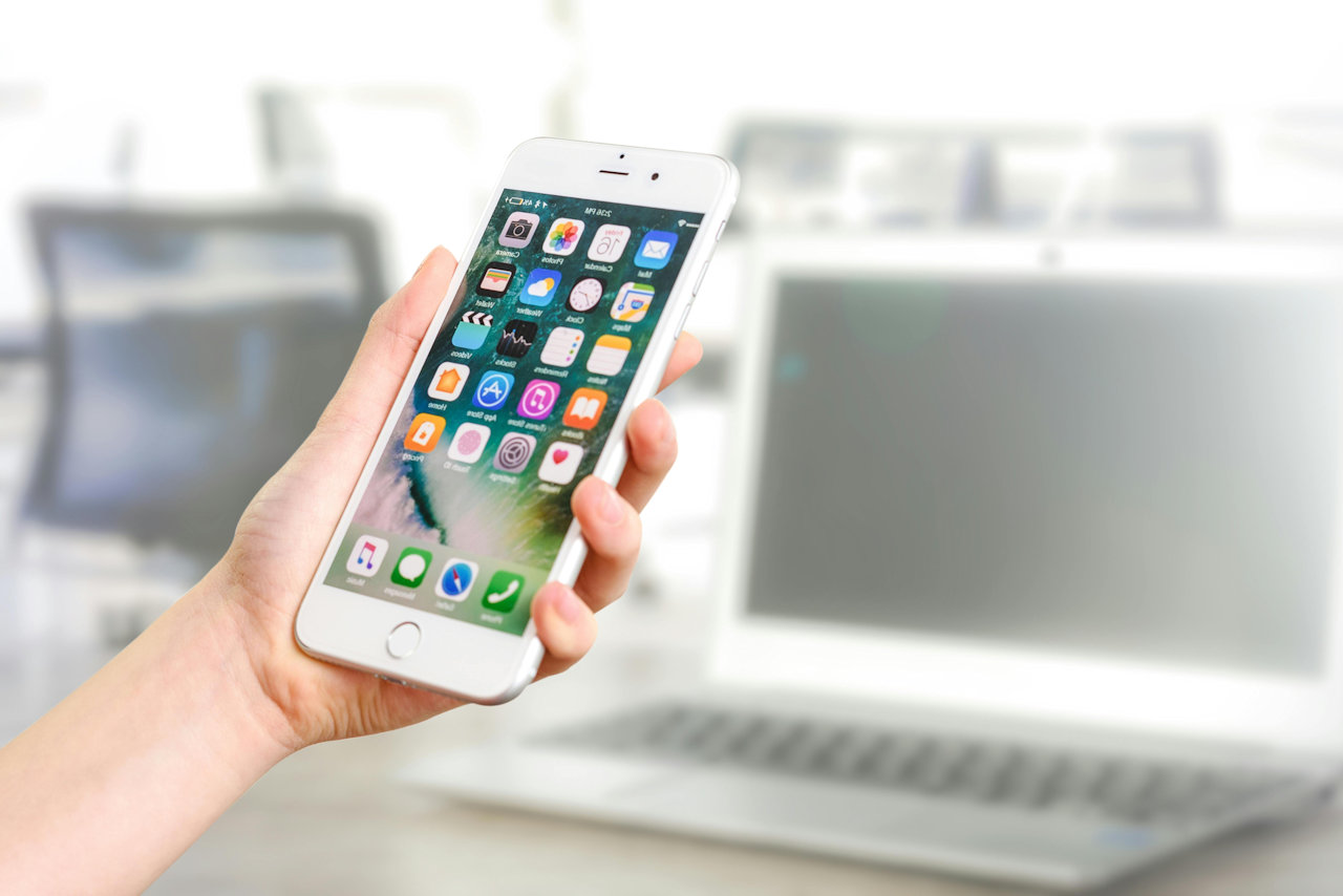 Hand holding a cell phone with a number of app icons on the screen.